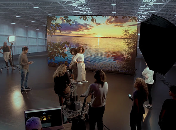 Professional XR studio production team filming two models on a VMX LED volume displaying a sunset lake background.